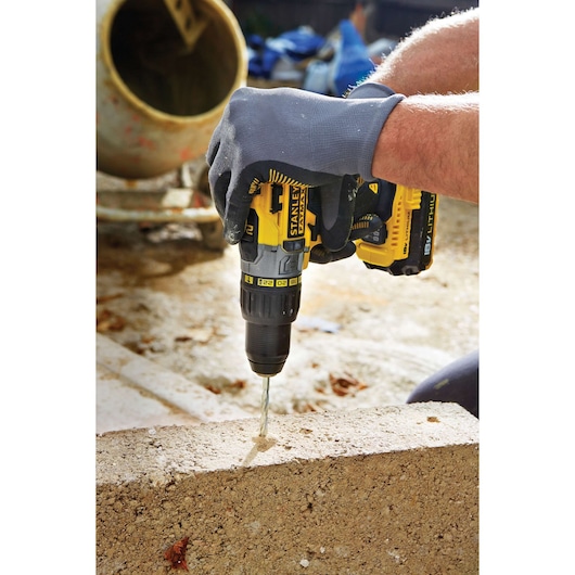 Photo of STANLEY FMC625M2S cordless drill, yellow and black, used for drilling into concrete block on construction site.