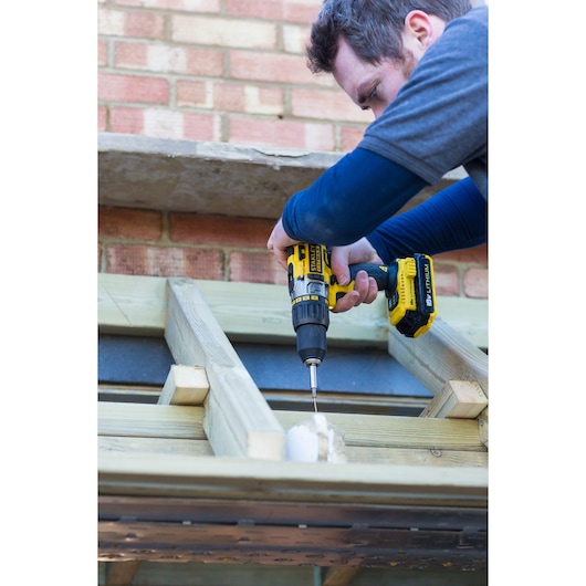 STANLEY FMC625M2S cordless drill in use screwing into wooden beams, construction setting, side angle.