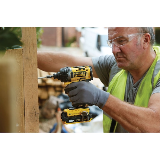 STANLEY FMC645D2 cordless impact driver being used outdoors on wooden construction, yellow and black design.