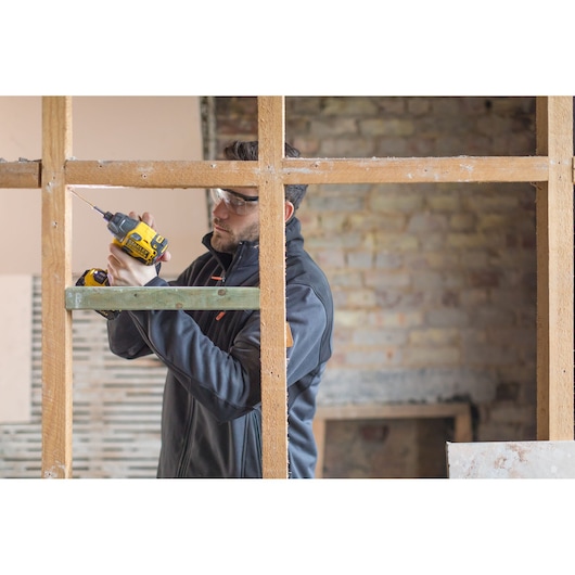 STANLEY FMC647D2 cordless drill in use drilling wood in construction setting, side angle photography.