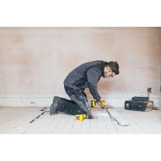 STANLEY FMC647D2 cordless drill in use, worker kneeling on wood floor, tool cases in background.