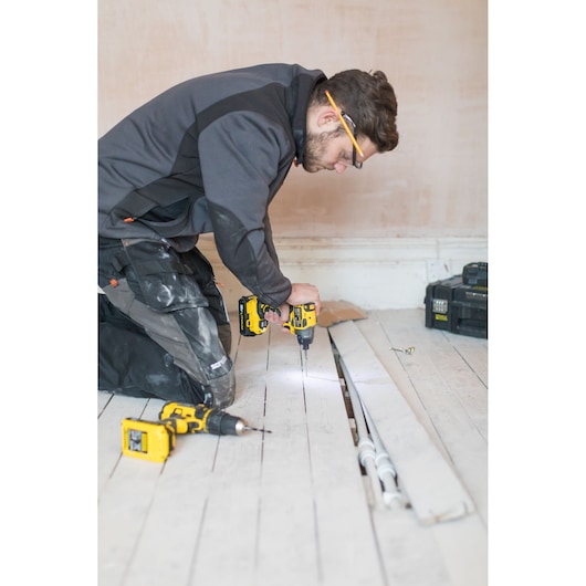 STANLEY FMC647D2 drill in use during floor installation, photo showing worker kneeling with tools and open floorboards.