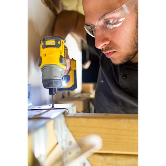 STANLEY FMC647D2 cordless impact driver in use, close-up, person wearing safety glasses driving screw in wood.