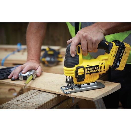 Photo of STANLEY FATMAX FMC650B cordless jigsaw in use cutting plywood, showing ergonomic grip and 18V lithium battery.