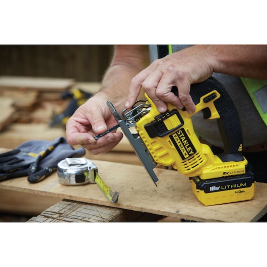 Photo of STANLEY FMC650B cordless jigsaw being fitted with a blade, close-up with work gloves and tape measure.