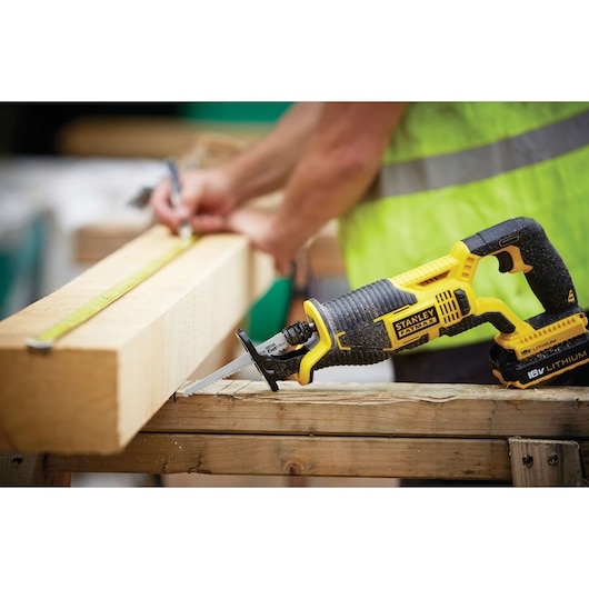 STANLEY FMC675D2 cordless reciprocating saw on wood beam, close-up with person measuring in background.