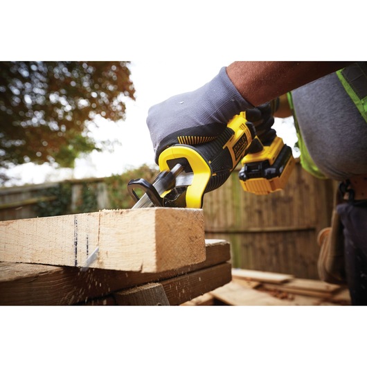 STANLEY FMC675D2 cordless reciprocating saw cutting wood outdoors, close-up of saw and gloved hand.