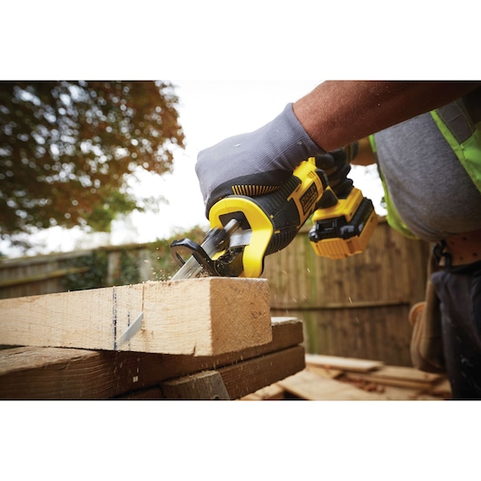 Photo of STANLEY FMC675D2 reciprocating saw cutting wood outdoors, worker wearing gloves.