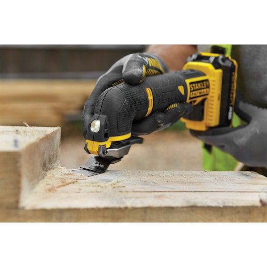 STANLEY FMC710B cordless multi-tool in use cutting wood, close-up of tool and gloved hand.