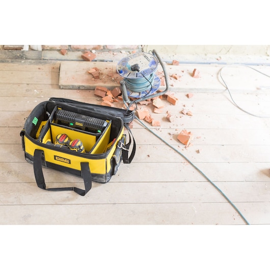 STANLEY FMCB100B yellow tool bag on wooden floor, open, holding tools and batteries, construction setting.