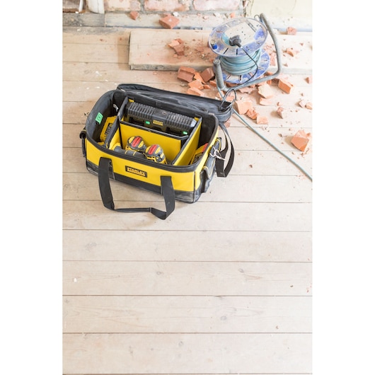 STANLEY FMCB100B tool bag with yellow and black design, open on worksite with tools and charger visible, top view.