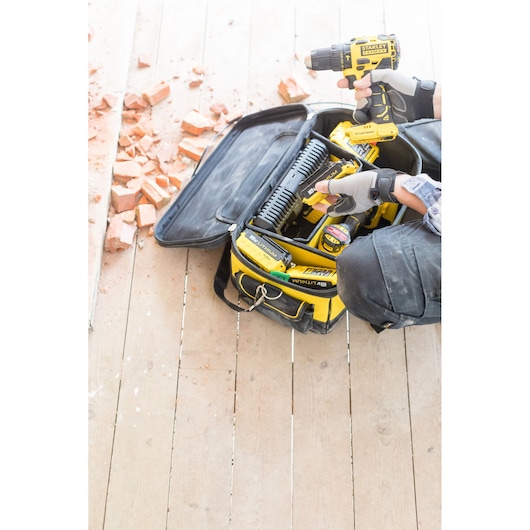 STANLEY FMCB100B cordless drill on wood floor with yellow-black tool bag, gloves, and broken bricks nearby.