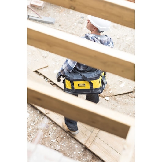 STANLEY FMCB100B tool bag in yellow and black carried by a worker at a construction site.