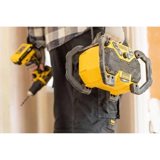 Stanley FMCR001B portable yellow jobsite radio held by worker in construction setting, partial view.