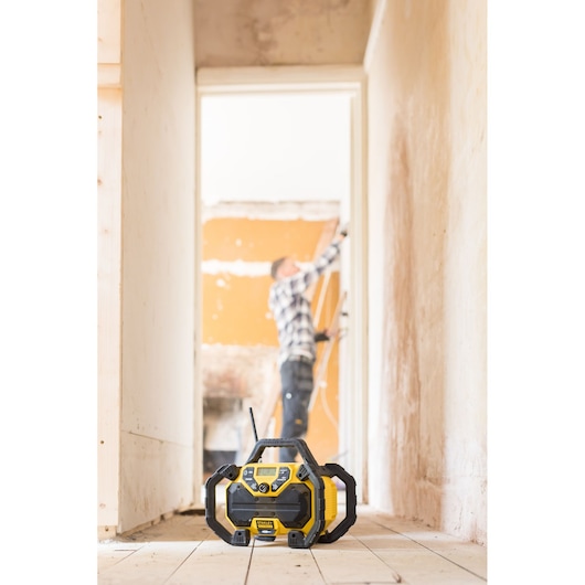 STANLEY FMCR001B jobsite radio on floor, foreground view, with worker blurred in background.