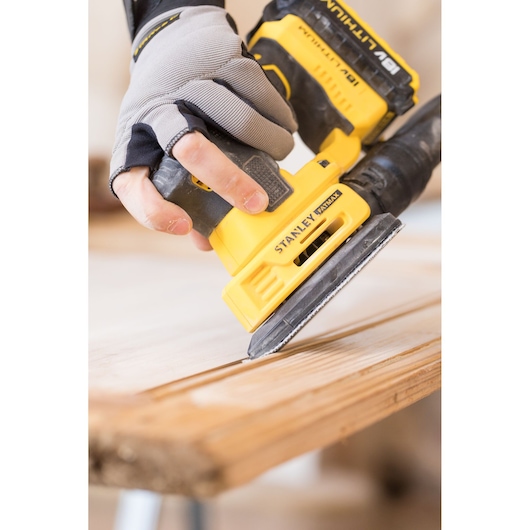 Photo of STANLEY FMCW210B cordless sander being used on wood surface, close-up angle.