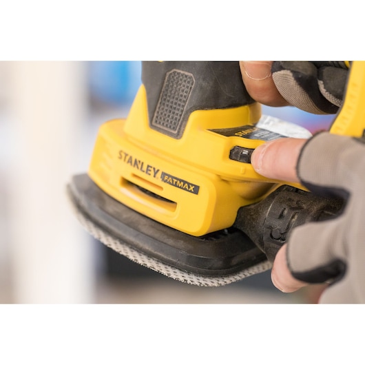 STANLEY FMCW210B palm sander close-up in use, yellow and black handheld power tool.
