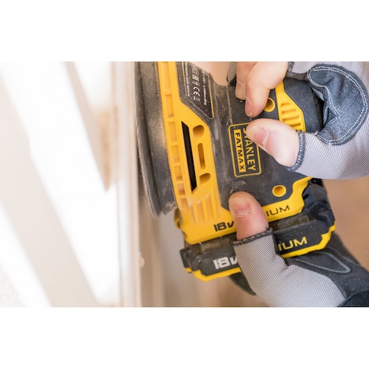 STANLEY FMCW220B cordless sander in use, yellow and black design, close-up on gloved hands.
