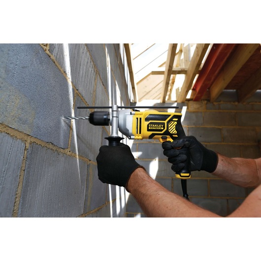 Photo of STANLEY FME140K hammer drill in use on a masonry wall, worker holds tool with black gloves.