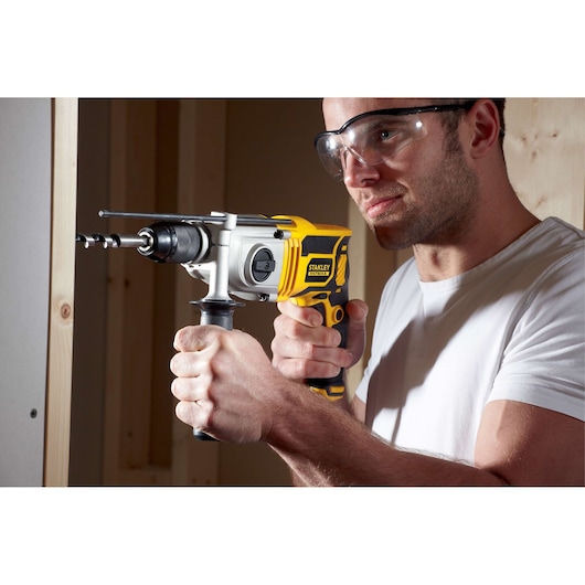Stanley FME142K hammer drill in use, yellow and black design, being operated on a wall indoors.