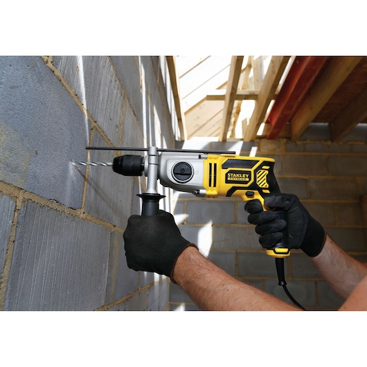 STANLEY FME142K hammer drill in use drilling into concrete wall, yellow and black body, side view.