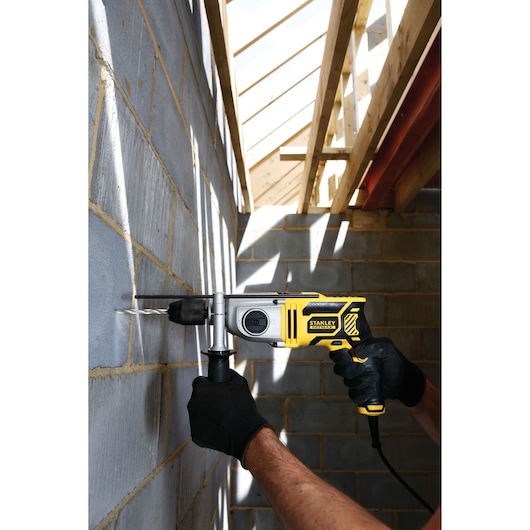 STANLEY FME142K corded hammer drill in use on masonry wall at construction site, shown from side angle.