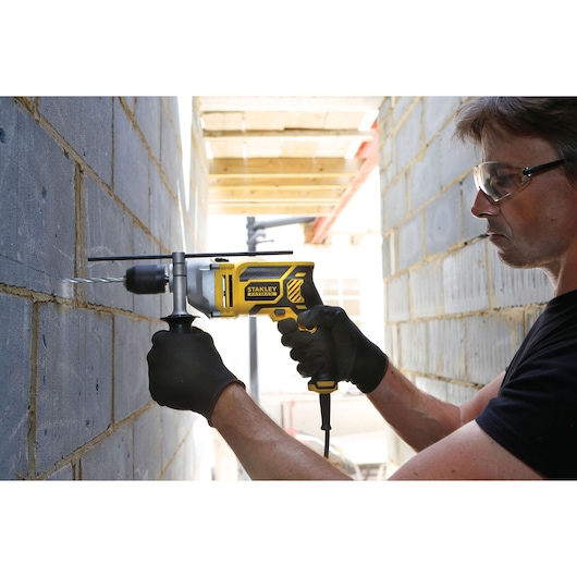 Photo of STANLEY FME142K corded drill being used to drill into a concrete wall, black and yellow design, side view.