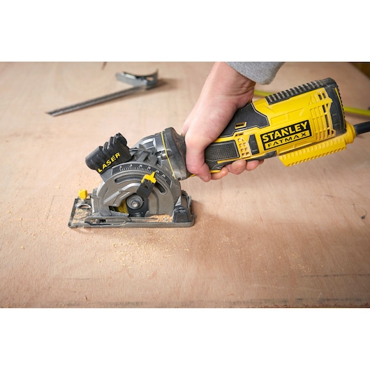 Photo of STANLEY FME380K handheld circular saw with laser cutting guide in use on wood surface.