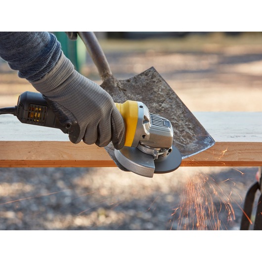 STANLEY FMEG220K angle grinder in use grinding a shovel blade, close-up with sparks flying.