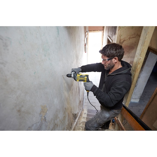STANLEY FMEH750K corded hammer drill in use drilling into wall, product photography, side angle.