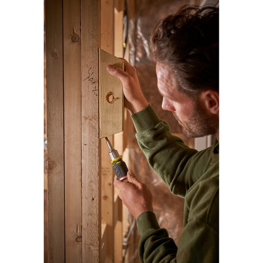 STANLEY FMHT0-62688 screwdriver used to fasten wood panel onto timber frame in indoor setting.