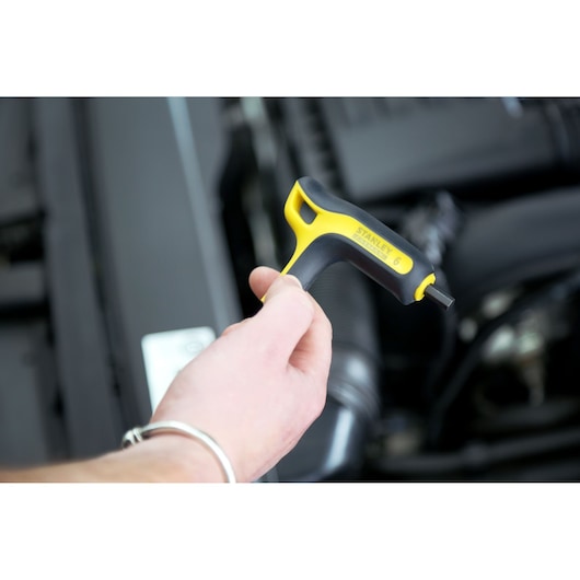 Stanley FMHT0-69049 hex key with yellow and black handle in hand near engine compartment.