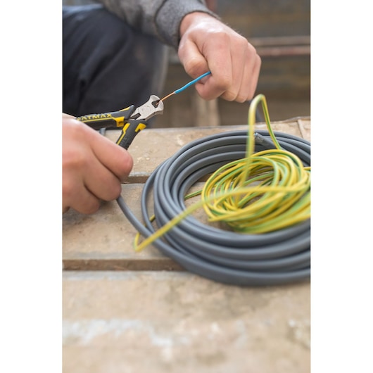 STANLEY FMHT0-80541 diagonal pliers cutting electrical wire, with coiled cables on a workbench.