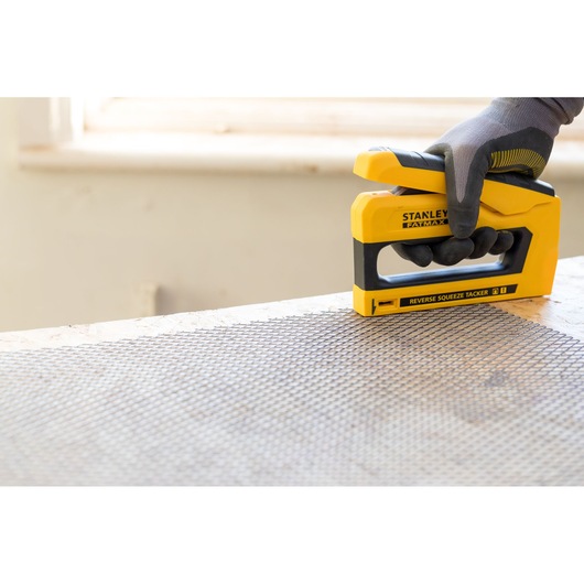 Stanley FMHT0-80551 stapler being used on wire mesh, close-up angle, yellow and black design.