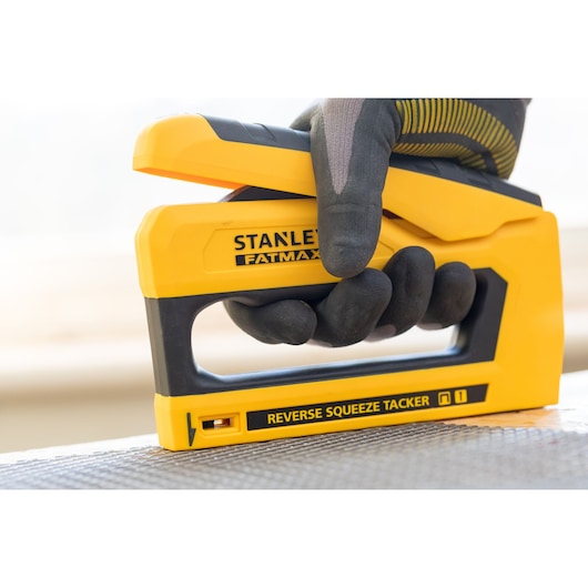 Photo of STANLEY FMHT0-80551 stapler, yellow and black, being used with a gloved hand on a surface.