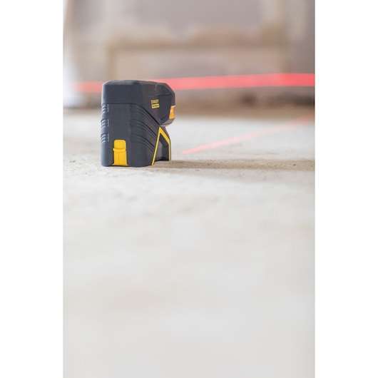 Stanley FMHT1-77415 cross line laser level on floor, side angle, projecting bright red laser lines.