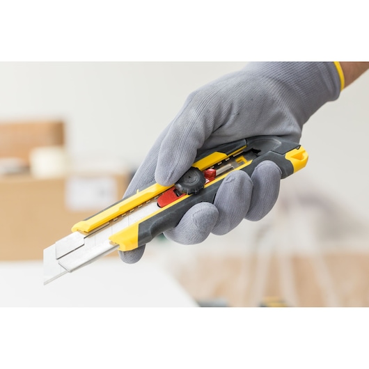 STANLEY FMHT10330-0 utility knife with yellow and black body, held in a gloved hand.