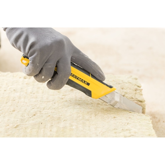 Photo of STANLEY FMHT10338-0 utility knife cutting insulation material, held by a gloved hand.