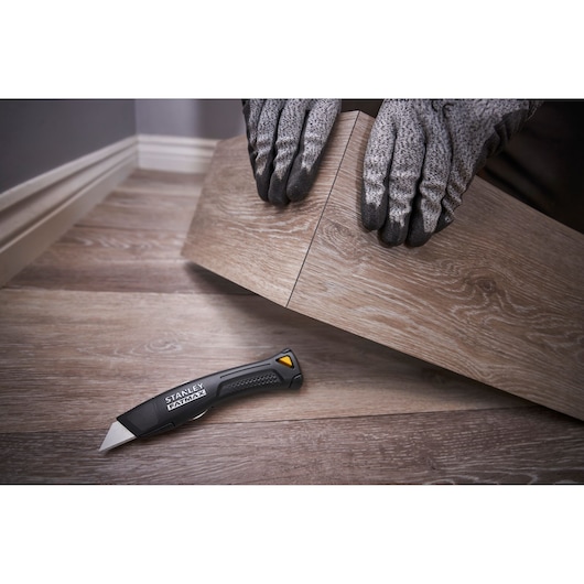 STANLEY FMHT10500-0 utility knife on wood floor, person with gloves installing vinyl flooring.