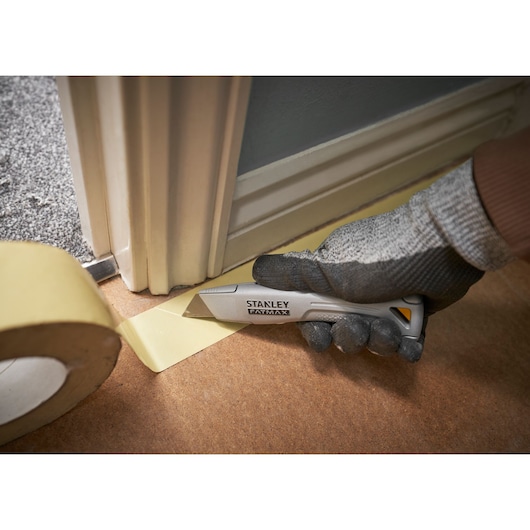 STANLEY FMHT10501-0 utility knife cutting tape near door frame, close-up photo with gloved hand.