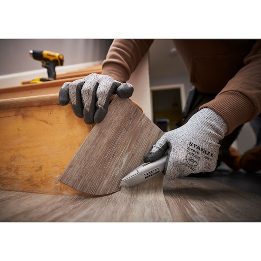 Photo of worker wearing gloves using STANLEY FMHT10501-0 utility knife to cut vinyl flooring.