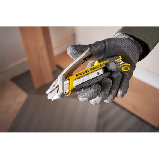 Photo of STANLEY FMHT10592-0 utility knife with yellow and black design held in gloved hand.