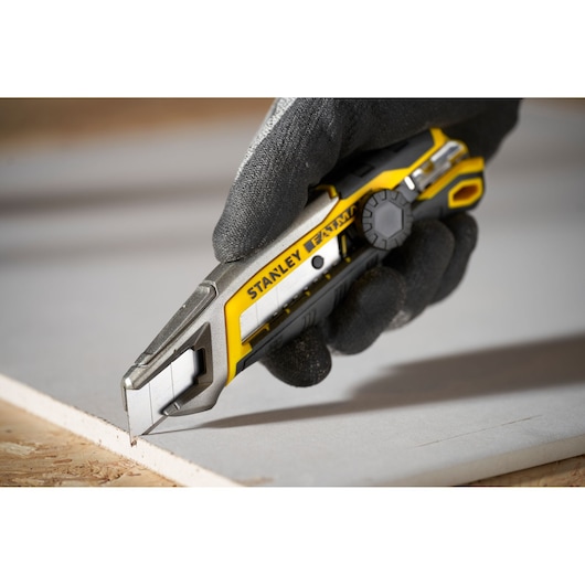 STANLEY FMHT10592-0 utility knife with yellow and silver body in use cutting construction board.