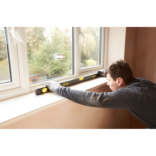 Stanley FMHT42447-1 spirit level used on windowsill by worker wearing gloves, indoor setting.