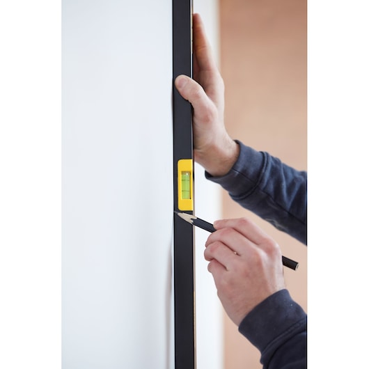 STANLEY FMHT42447-1 level tool held against wall, yellow bubble vial visible, hand marking line.