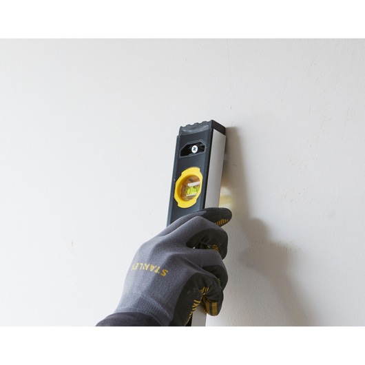 Photo of STANLEY FMHT42447-1 spirit level held by gloved hand against a wall, product in use.