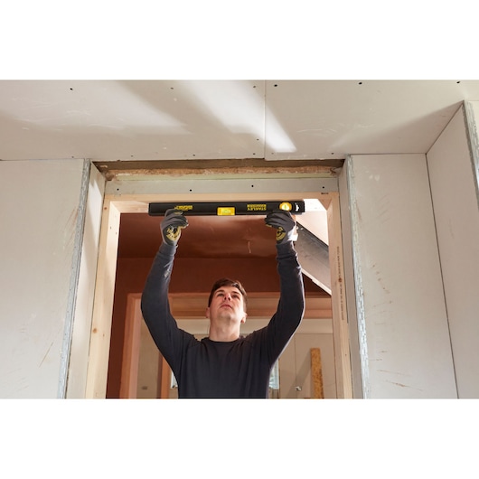 Person using STANLEY FMHT42554-1 spirit level to check doorway alignment during construction.