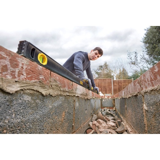 STANLEY FMHT42561-1 spirit level in use on brick wall construction, outdoor angle.
