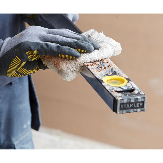 Photo of a gloved hand cleaning a STANLEY FMHT42561-1 level tool covered with debris, close-up view.