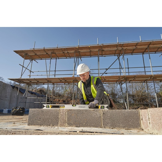 STANLEY FMHT43674-1 spirit level used by a worker on a construction site, photographed outdoors.